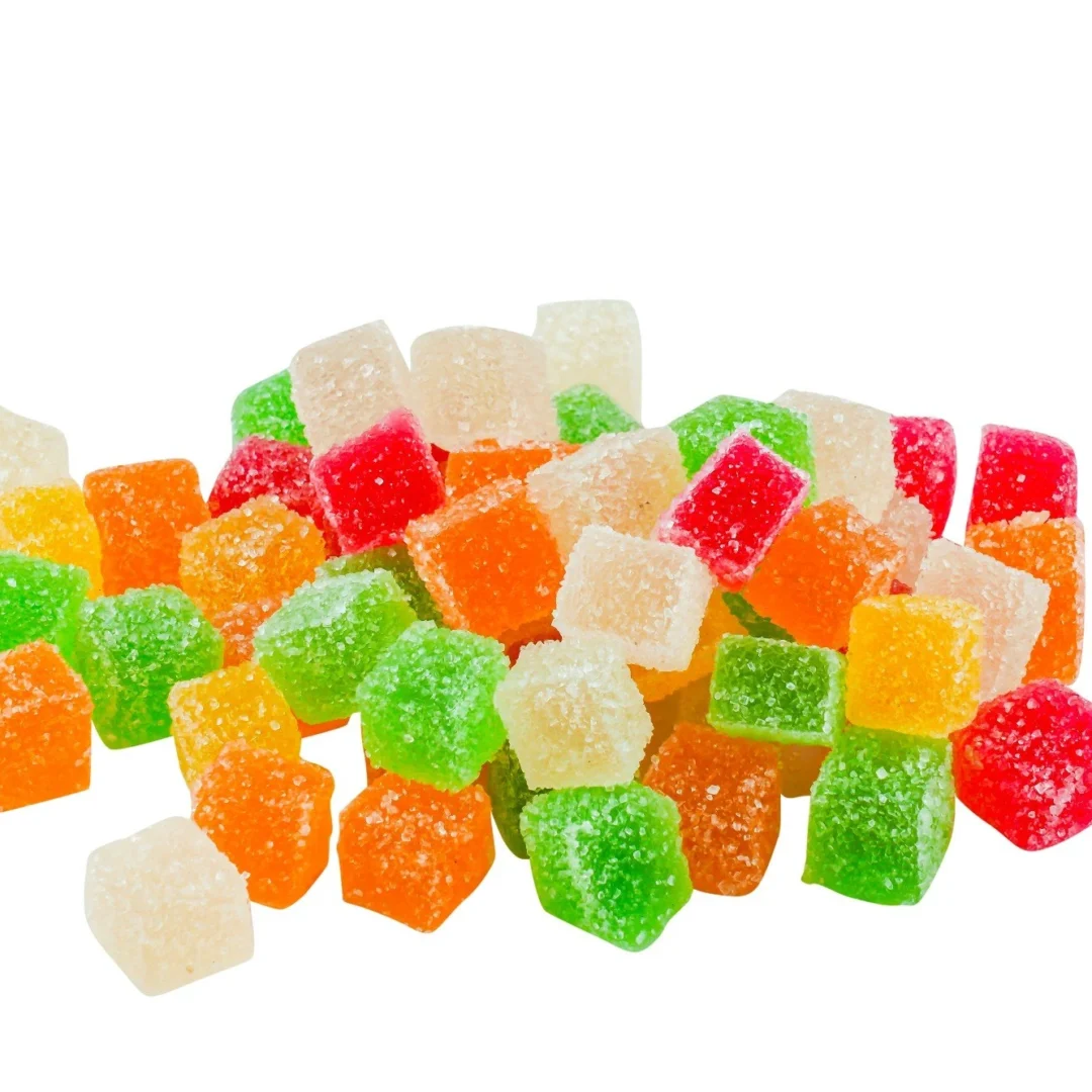 Pile of assorted colourful kratom gummies in cube shapes with sugar coating, featuring green, red, orange, and translucent hues, displayed on a white background.