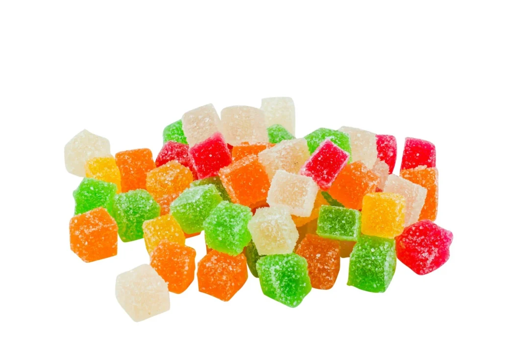 Pile of assorted colourful kratom gummies in cube shapes with sugar coating, featuring green, red, orange, and translucent hues, displayed on a white background.